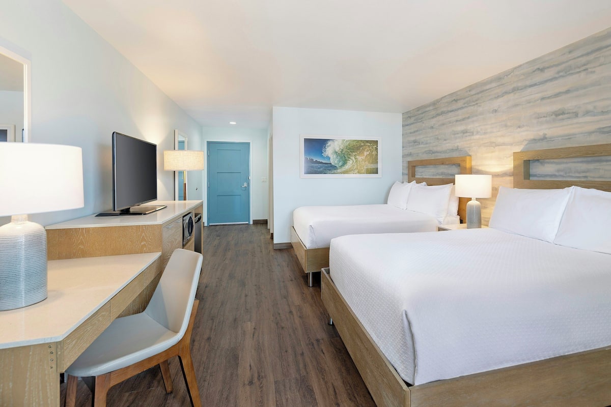 Une chambre d’hôtel avec deux lits, un bureau et une chaise, une télévision et une salle de bain.