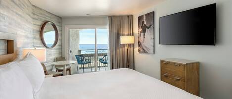 Una habitación de hotel con una cama, un escritorio con sillas, un televisor y vista al océano.