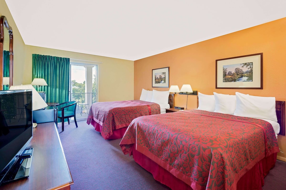 A hotel room with two beds, a desk, a chair, a TV, and two lamps.
