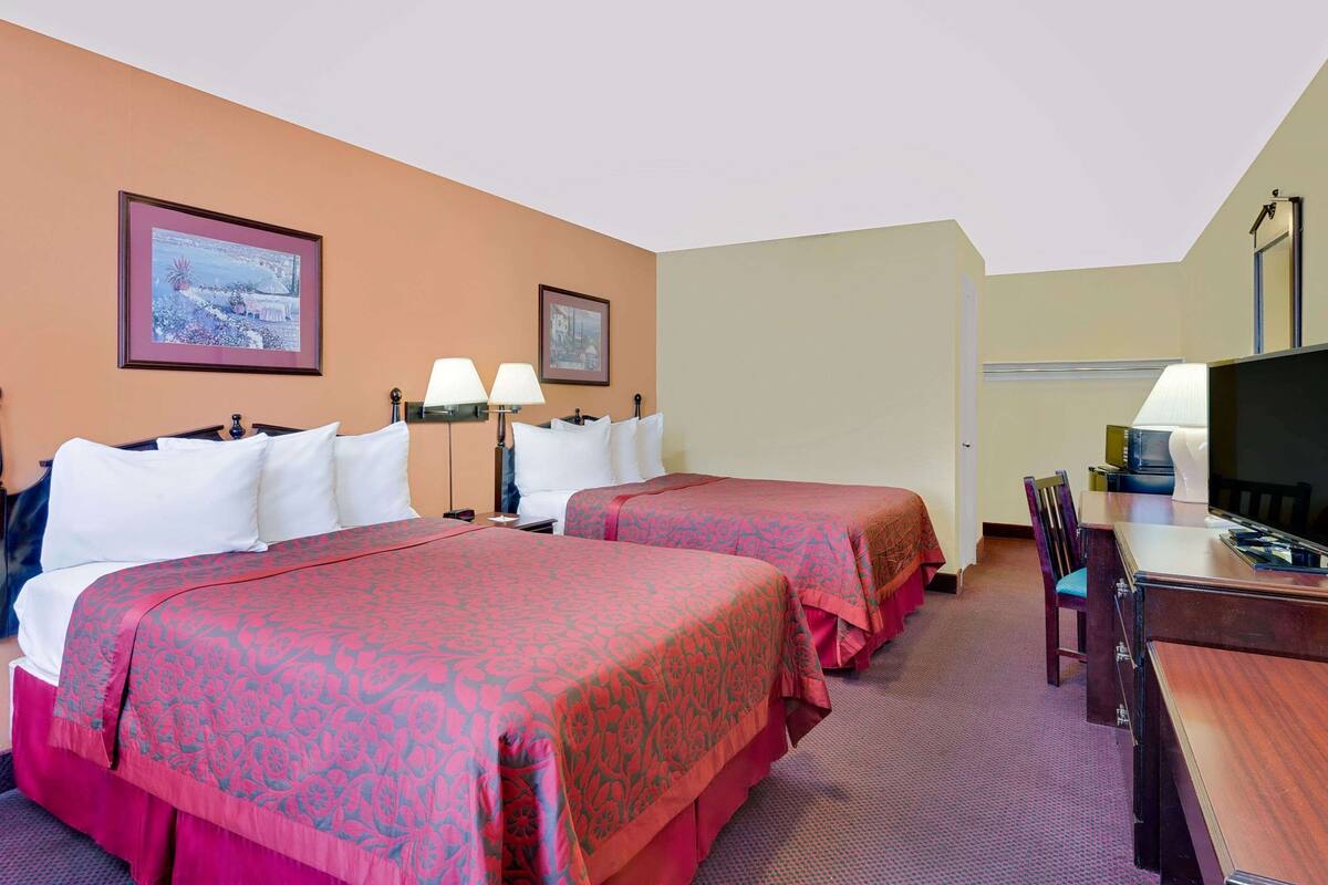 A hotel room with two beds, a desk, a chair, and a television.