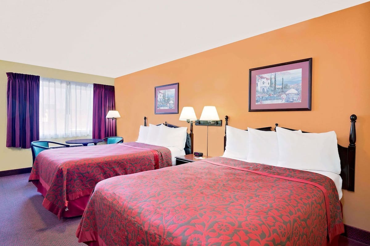 A hotel room with two beds, a desk, a chair, and two lamps.