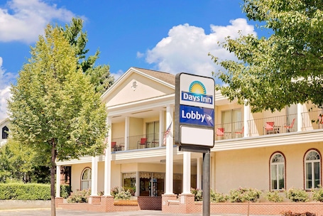 A Days Inn lobby with a white facade, multiple windows, and a balcony with red chairs.