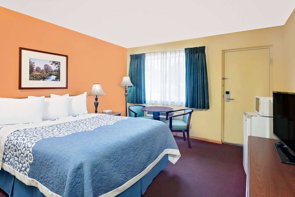 A hotel room with a large bed, a desk with a chair, a television, and a window with curtains.