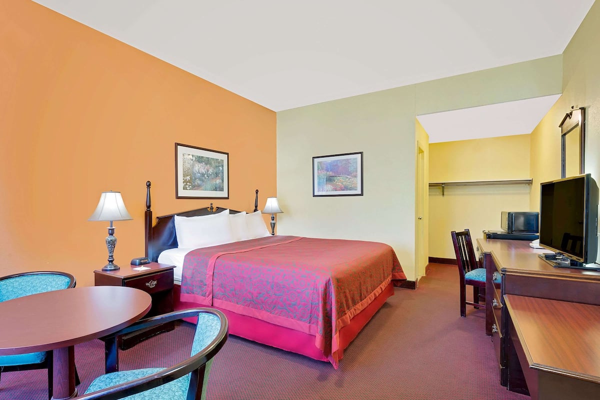 A hotel room with a bed, two bedside tables with lamps, a desk with a chair, a television, and two framed pictures on the wall.