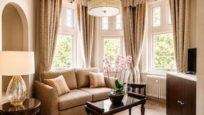A living room with a sofa, coffee table, lamp, and orchid plant. - Macdonald Berystede Hotel & Spa (Ascot)
