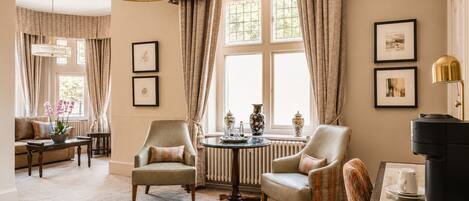 A room with two armchairs, a round table, a radiator, and a black cabinet with a coffee maker.