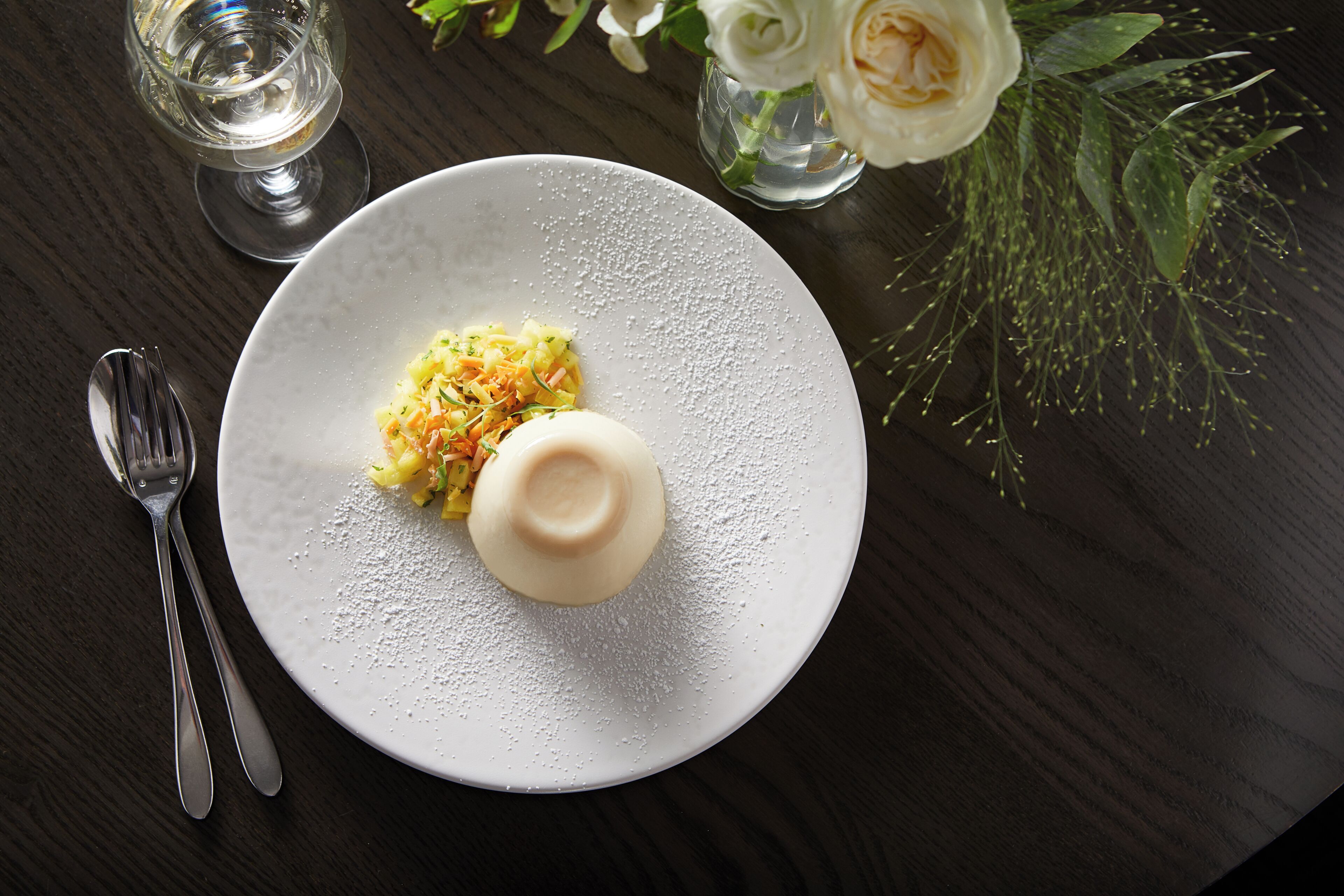 A plate with a dessert, a fork, and a glass of water on a dark wooden table.