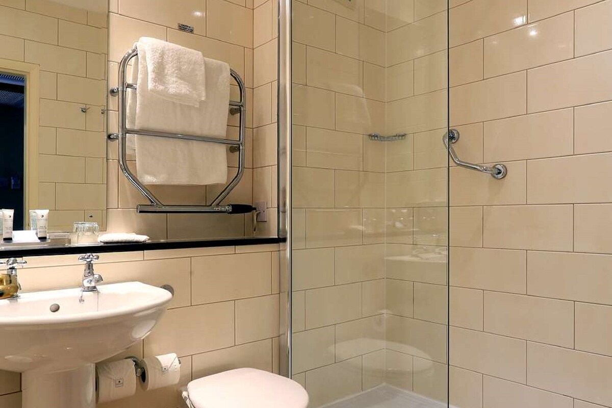 Un baño moderno con ducha envuelta en vidrio, lavamanos pedestal y retrete.