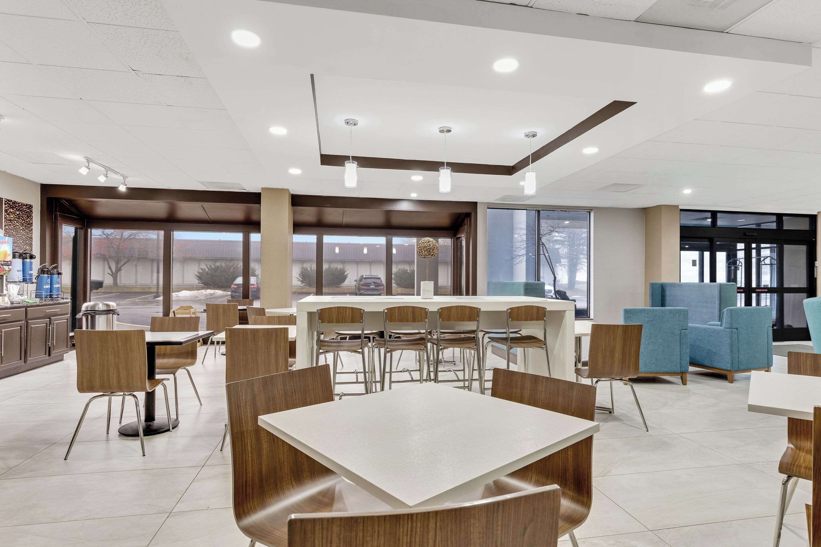 A modern dining area with multiple tables and chairs, large windows, and a counter with a coffee machine.