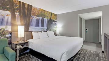 Una habitación de hotel con una cama grande, una mesita de noche con lámpara, una silla verde y un mural en la pared con una cascada.