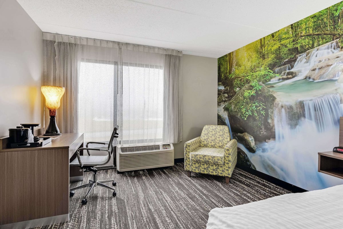A hotel room with a desk, chair, air conditioning unit, and a large mural of a waterfall.