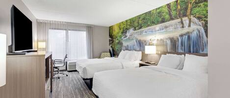 A hotel room with two beds, a desk, a TV, and a mural of a waterfall.