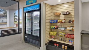Un rayon d'épicerie avec un présentoir réfrigéré pour les boissons et des étagères remplies de collations et de boissons.