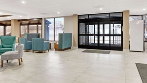 Un hall d’entrée avec des fauteuils turquoise, un pouf à motifs et une porte d’entrée en verre.