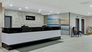 Un espace d’accueil au design moderne, comprenant un comptoir de réception, une enseigne murale et une fresque représentant un coucher de soleil sur une étendue d’eau.