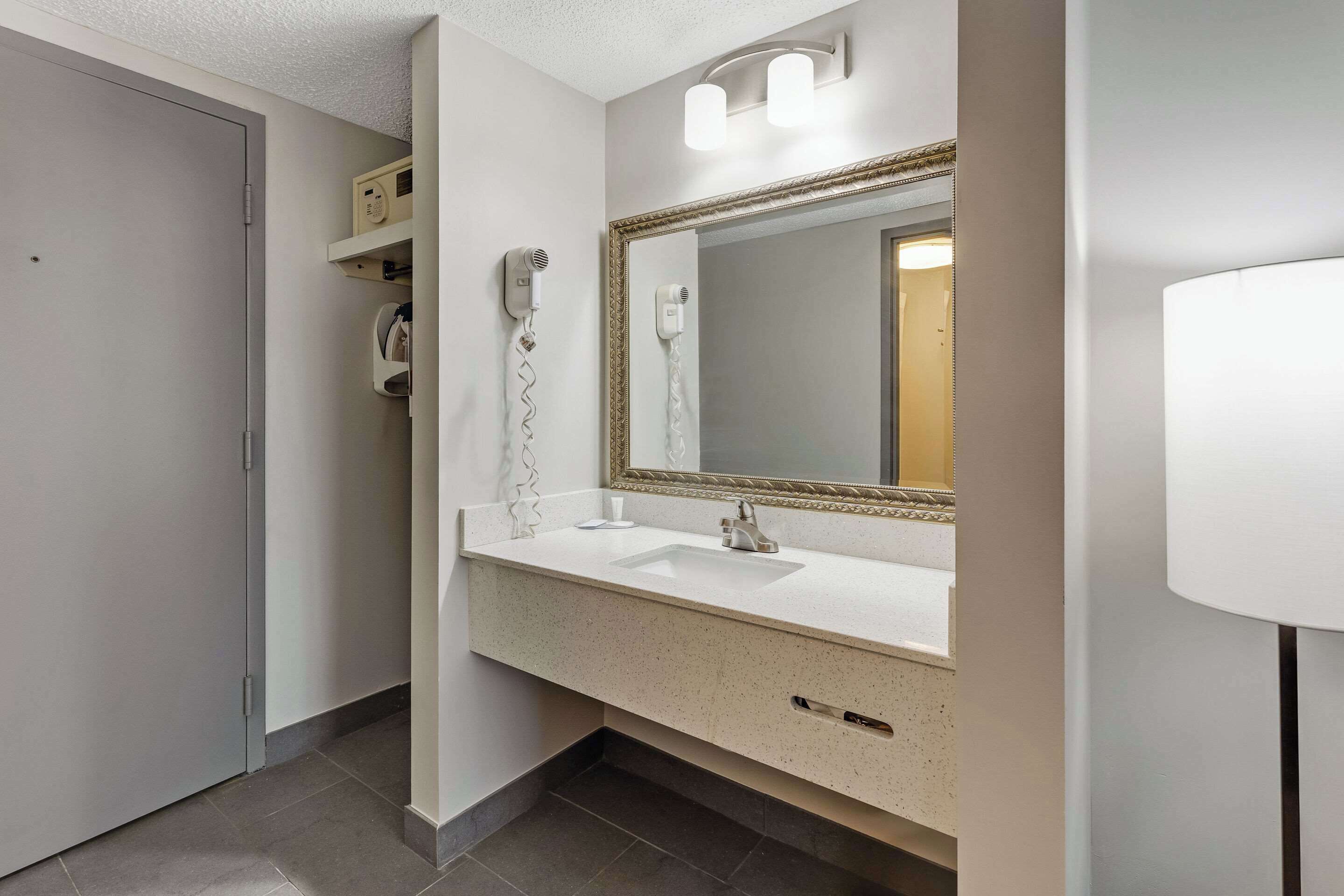A modern bathroom with a white sink, a large mirror with a gold frame, and a hairdryer mounted on the wall.
