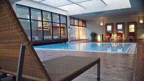 Une piscine intérieure avec des parois en verre transparent, un espace détente avec des fauteuils et une vue sur l’extérieur.