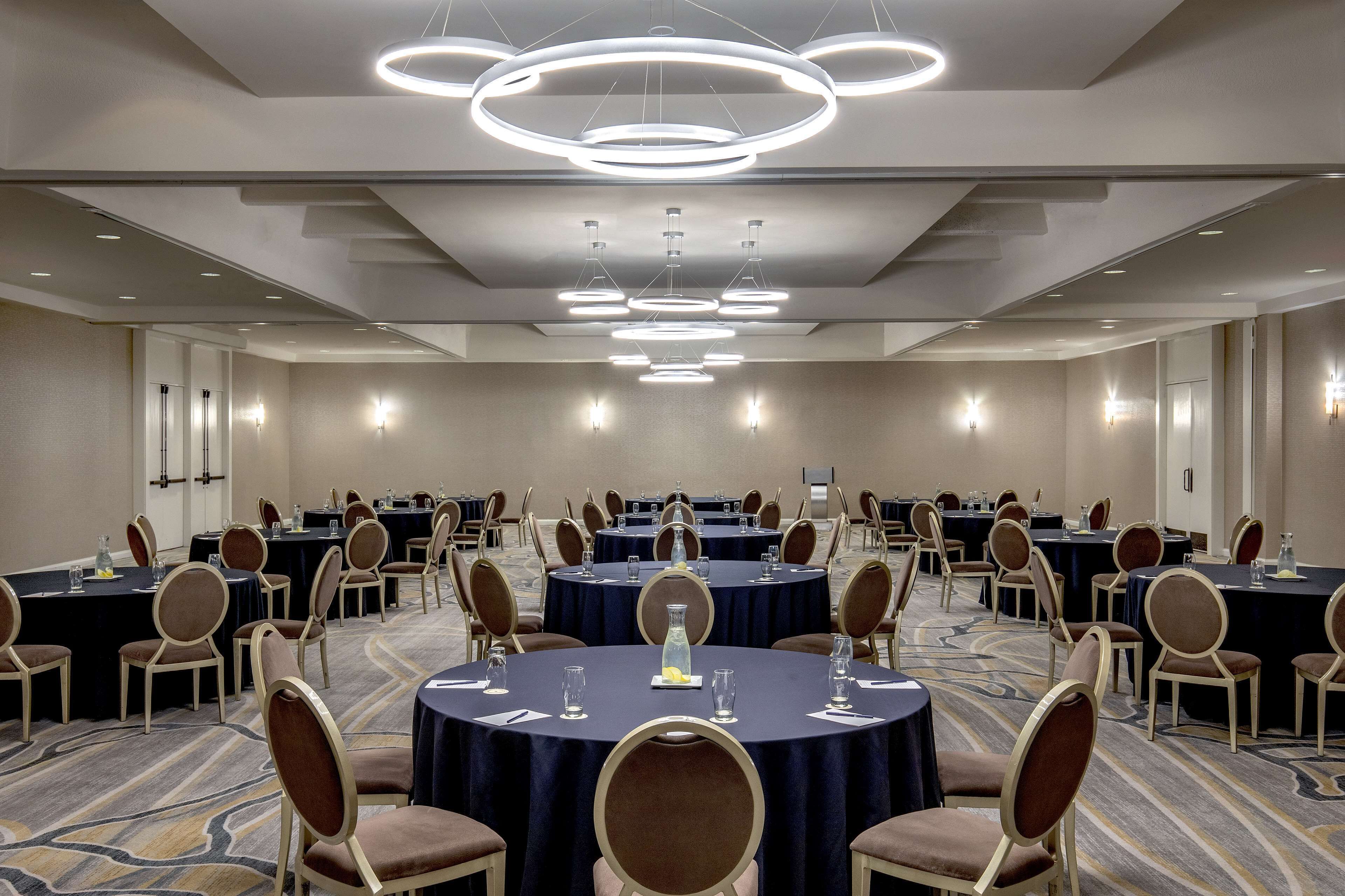 A conference room with multiple round tables, chairs, and overhead lighting.