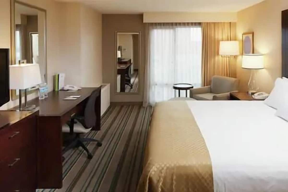 A hotel room with a bed, desk, chair, lamp, and a small table.