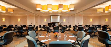 A conference room with round tables, black chairs, and a large screen.