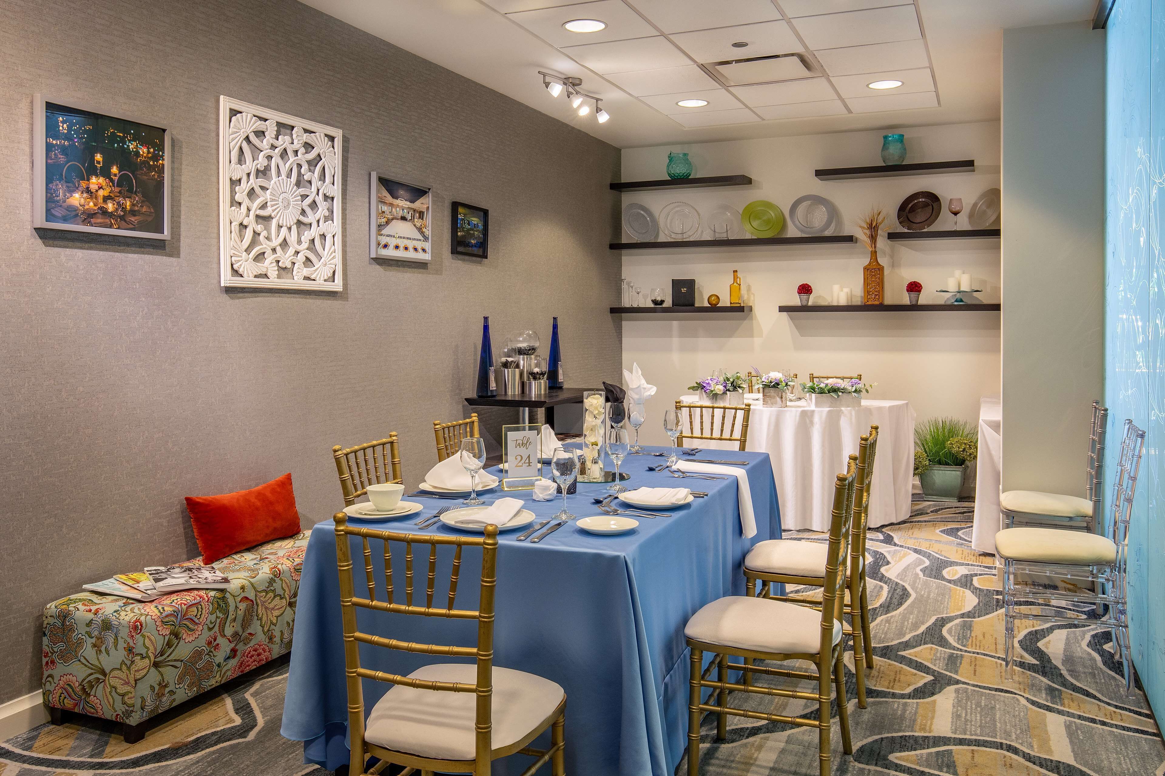 A dining area with a blue tablecloth, gold chairs, and a small sofa with a colorful cushion.