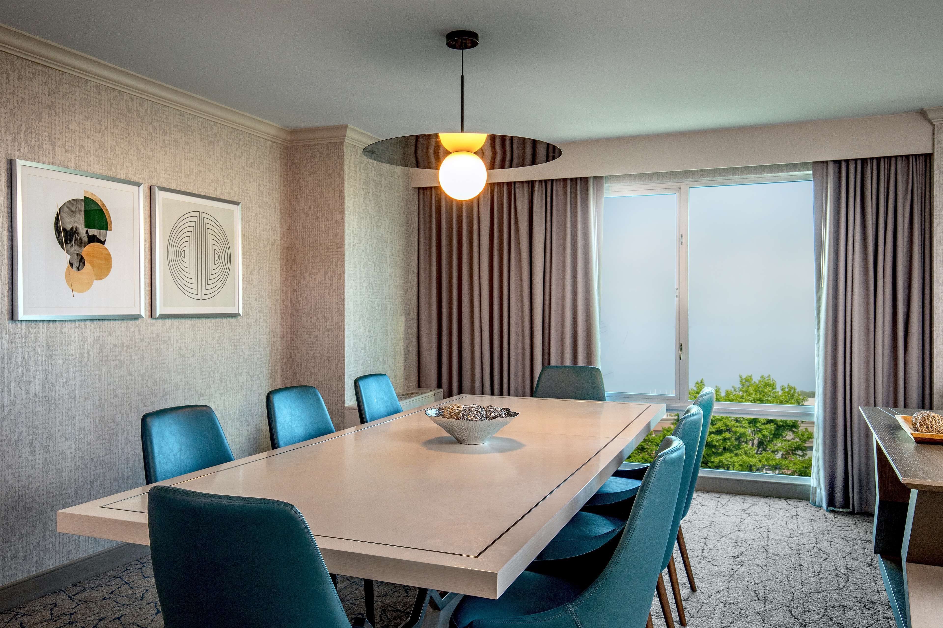 Un comedor moderno con una mesa larga, sillas azules y un bol de galletas. Hay obras de arte enmarcadas en la pared y vistas a zonas verdes por la ventana.