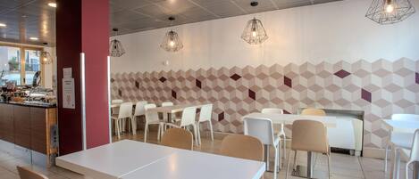 A modern dining area with white tables and chairs, geometric patterned walls, and pendant lighting.