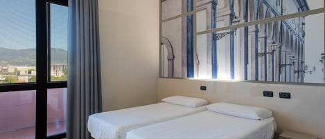 Habitación de hotel con dos camas, un ventanal con vistas, un cuadro en la pared y una mesita de noche.