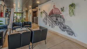A lobby with seating, a mural of a building, and hanging plants.