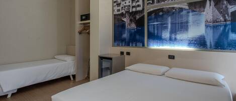 Habitación de hotel con dos camas individuales, un escritorio pequeño, un armario y un mural grande en la pared que muestra un puente sobre el agua.