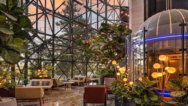 A spacious lobby with a high ceiling, modern seating, and a large glass enclosure with ambient lighting.
