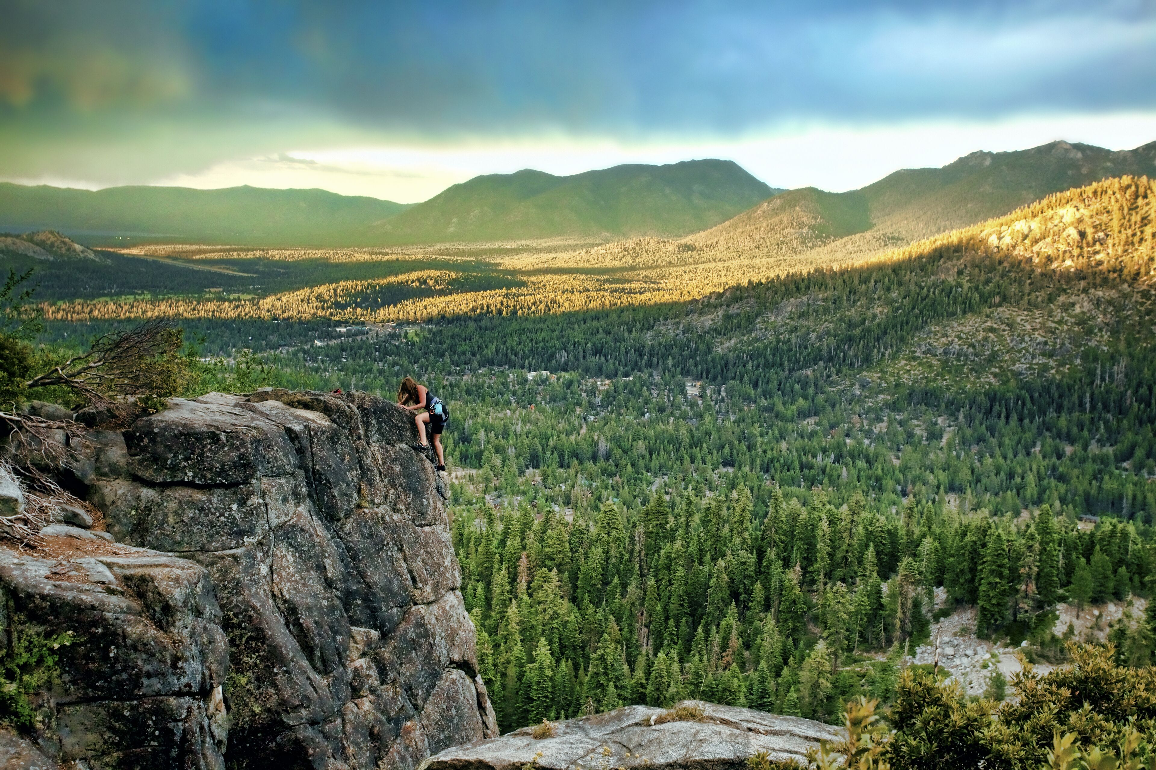 A person standing on a rock ledge overlooking a forested valley with mountains in the background.