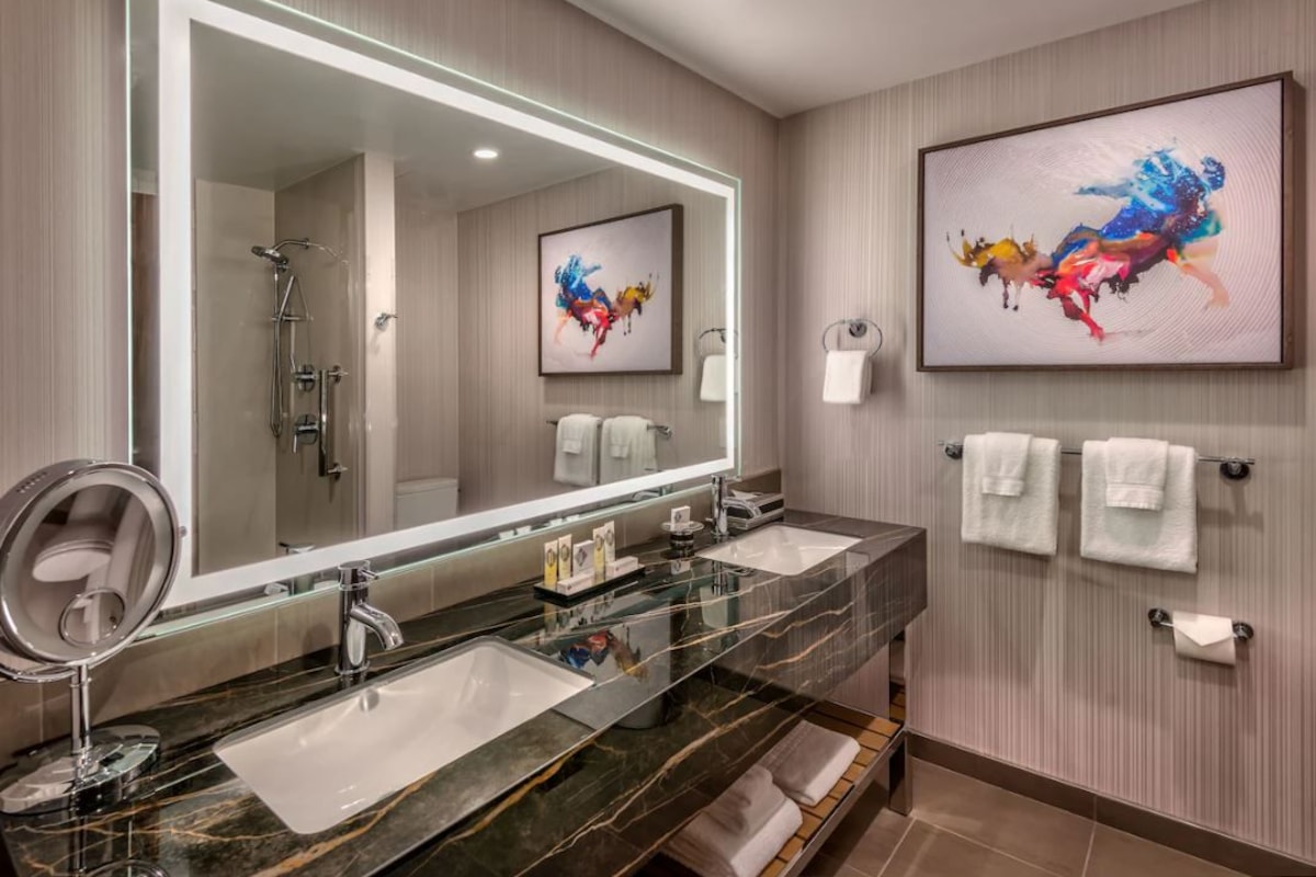 A modern bathroom with a large mirror, two sinks, a shower, and a towel rack.