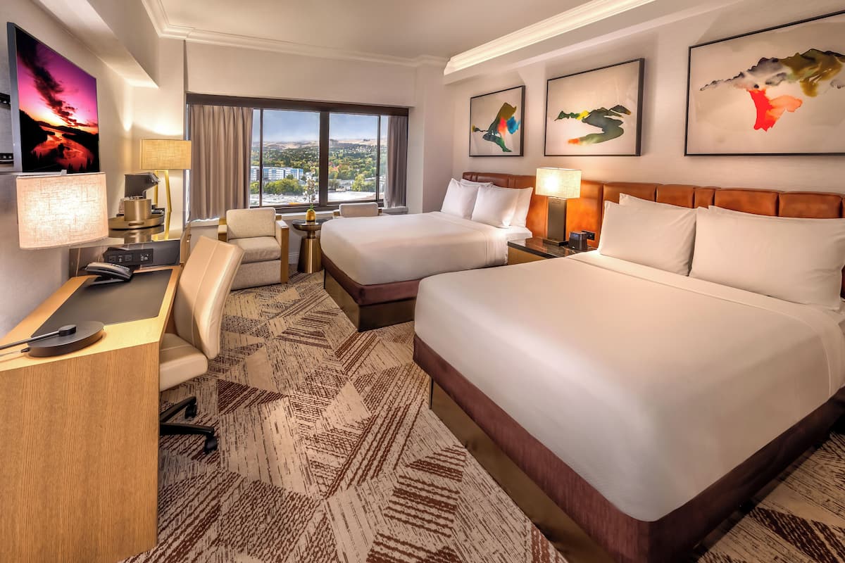 A hotel room with two beds, a desk, a chair, a TV, and artwork on the walls.