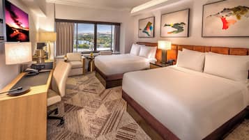 Quarto de hotel com duas camas, uma escrivaninha, uma cadeira, televisão e obras de arte nas paredes.