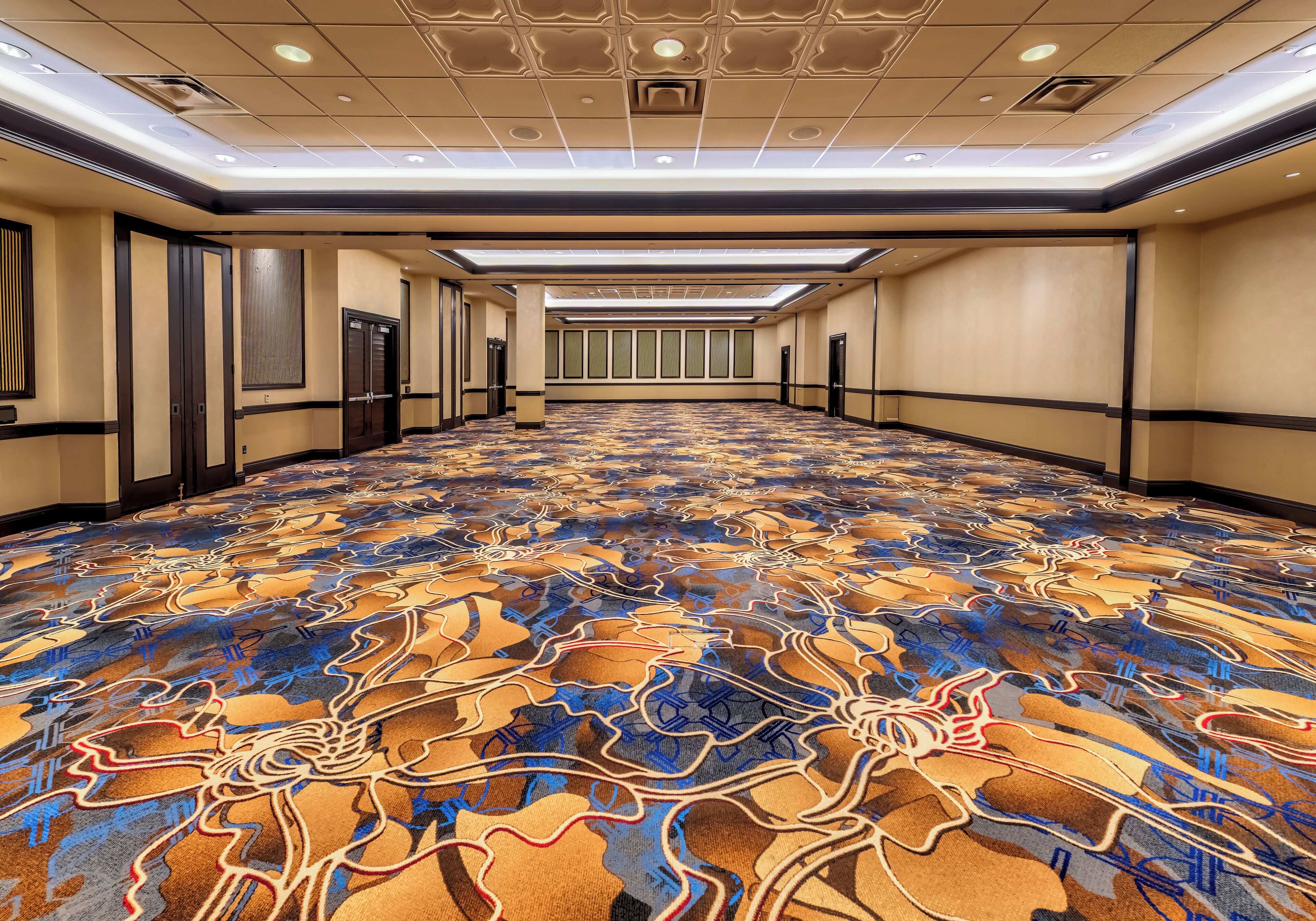 Un pasillo de hotel con alfombra estampada, puertas y un tragaluz.