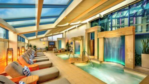 A spa area with sun loungers, a hot tub, and a glass-enclosed ceiling.