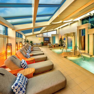 A spa area with sun loungers, a hot tub, and a glass-enclosed ceiling.