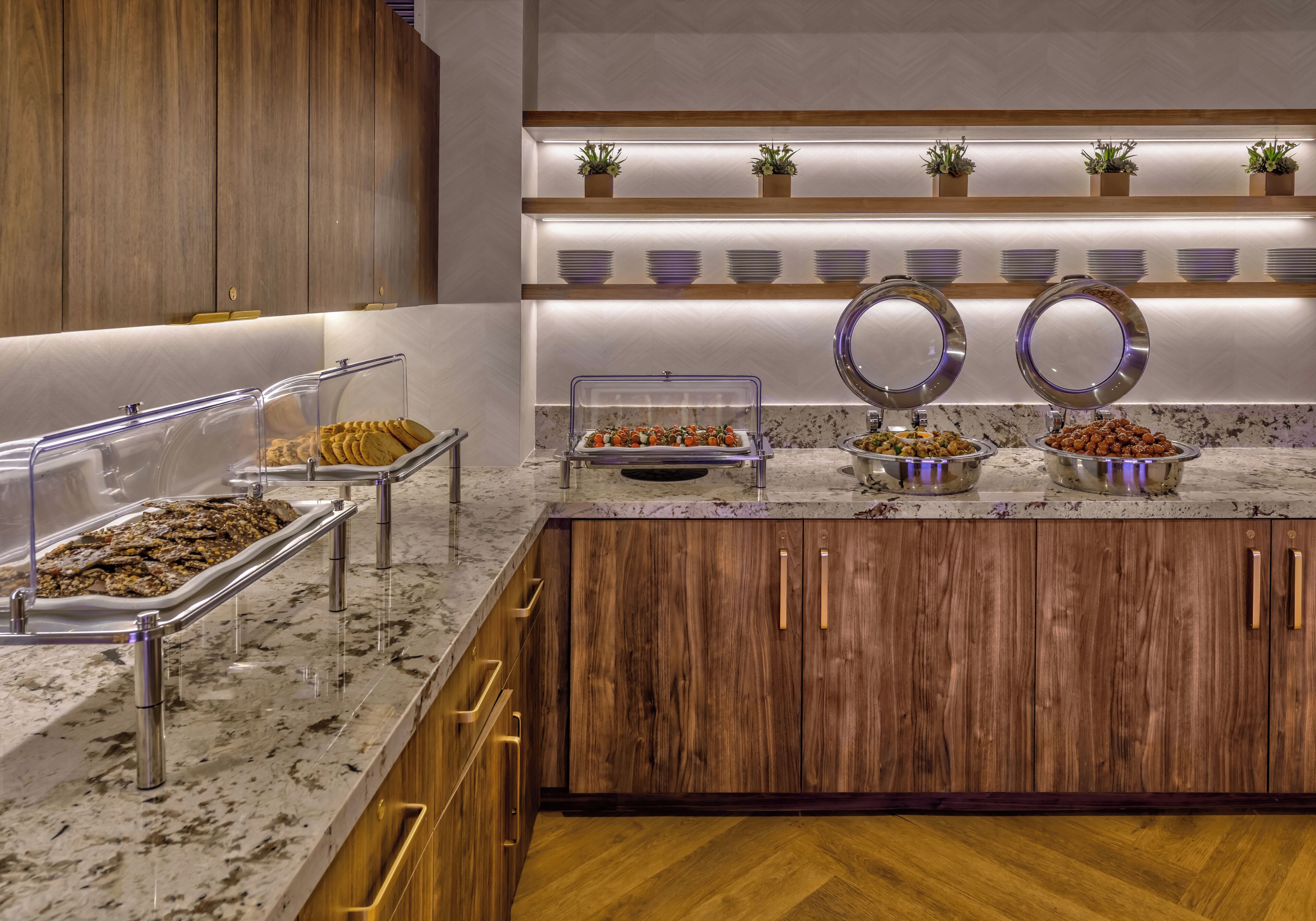 Zona de buffet amb diferents espais de menjar, armaris de fusta i una superfície de marbre.