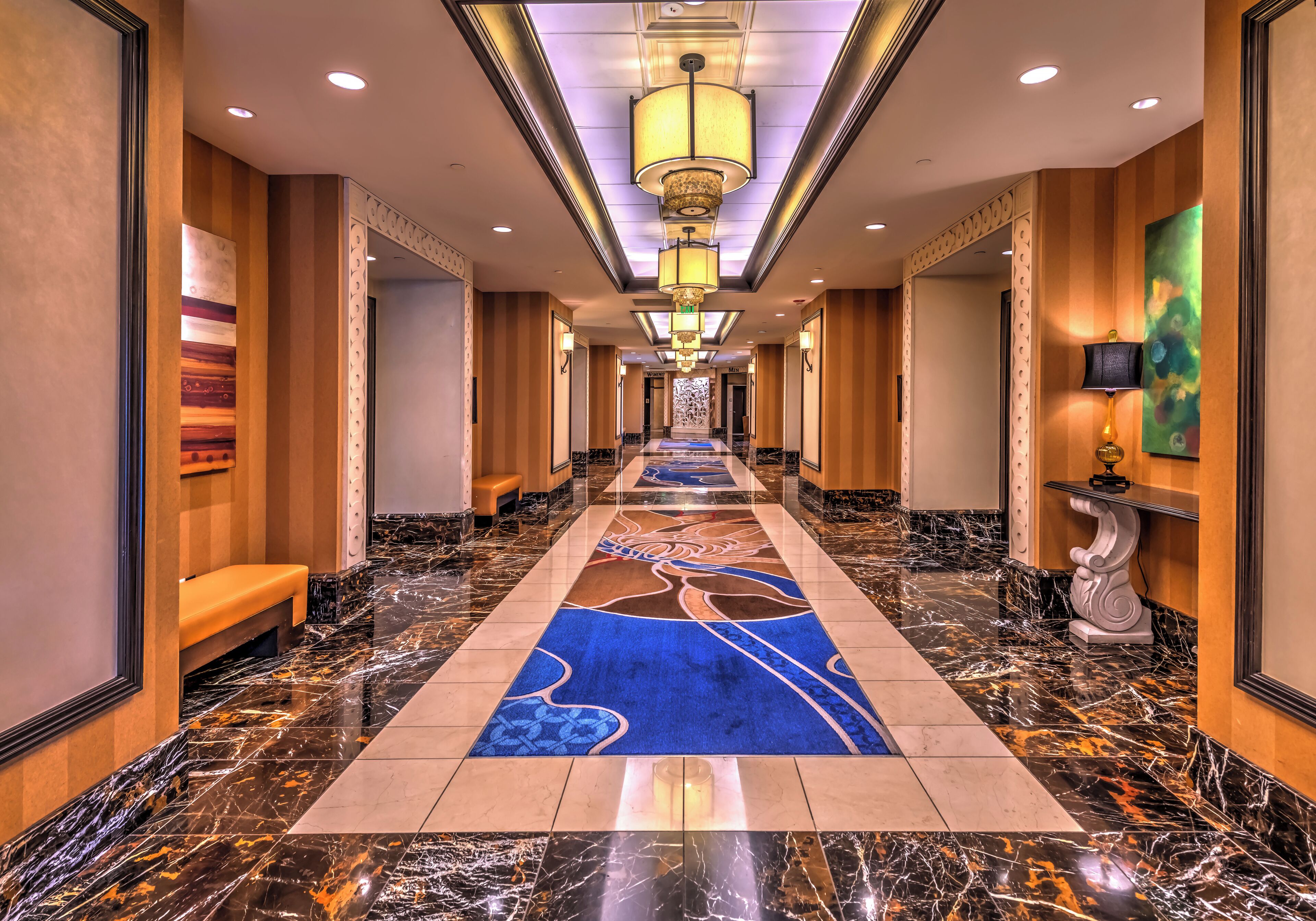 A hotel corridor with a marble floor, a blue carpet runner, and a chandelier.