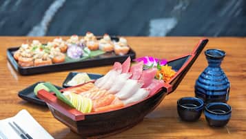 A wooden boat-shaped dish with various types of sushi and sashimi, accompanied by small black cups and a blue vase on a wooden table.