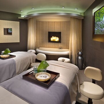 A spa room with two massage beds, a large bathtub, and a wall-mounted TV.
