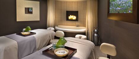 A spa room with two massage beds, a large bathtub, and a wall-mounted TV.