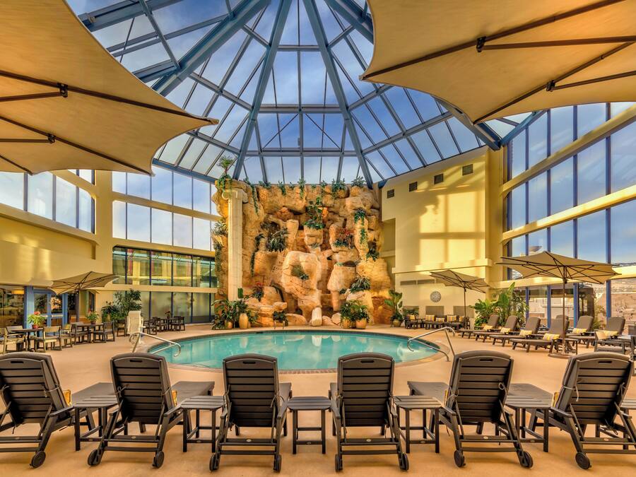 A pool area with lounge chairs, a glass ceiling, and a rock wall with plants.