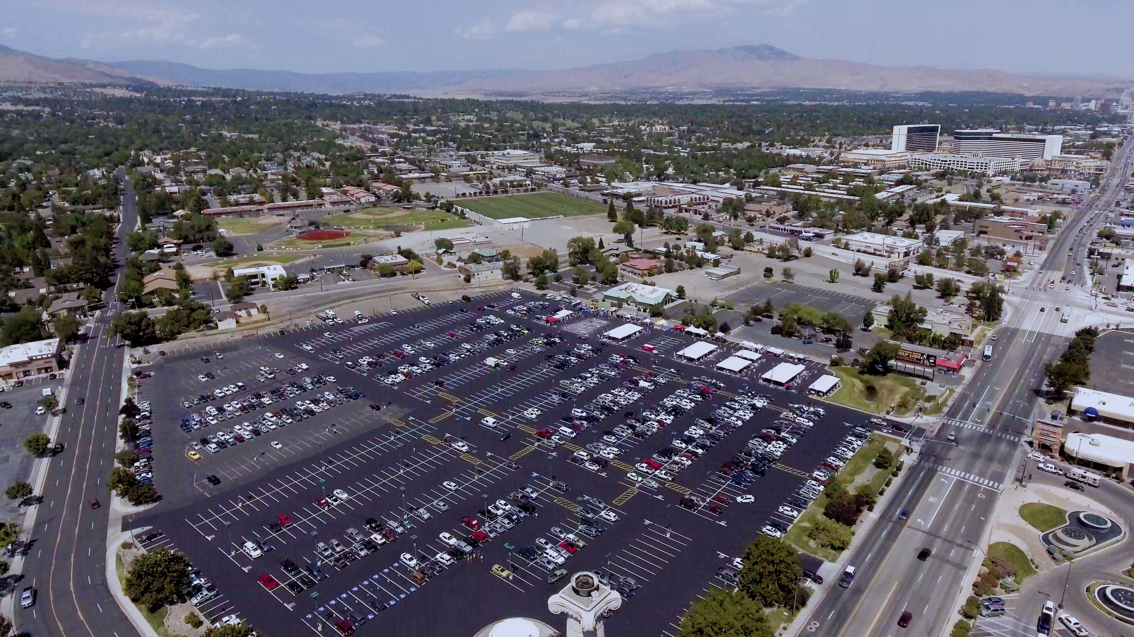 A large parking lot with multiple rows of parked cars, surrounded by roads and buildings.