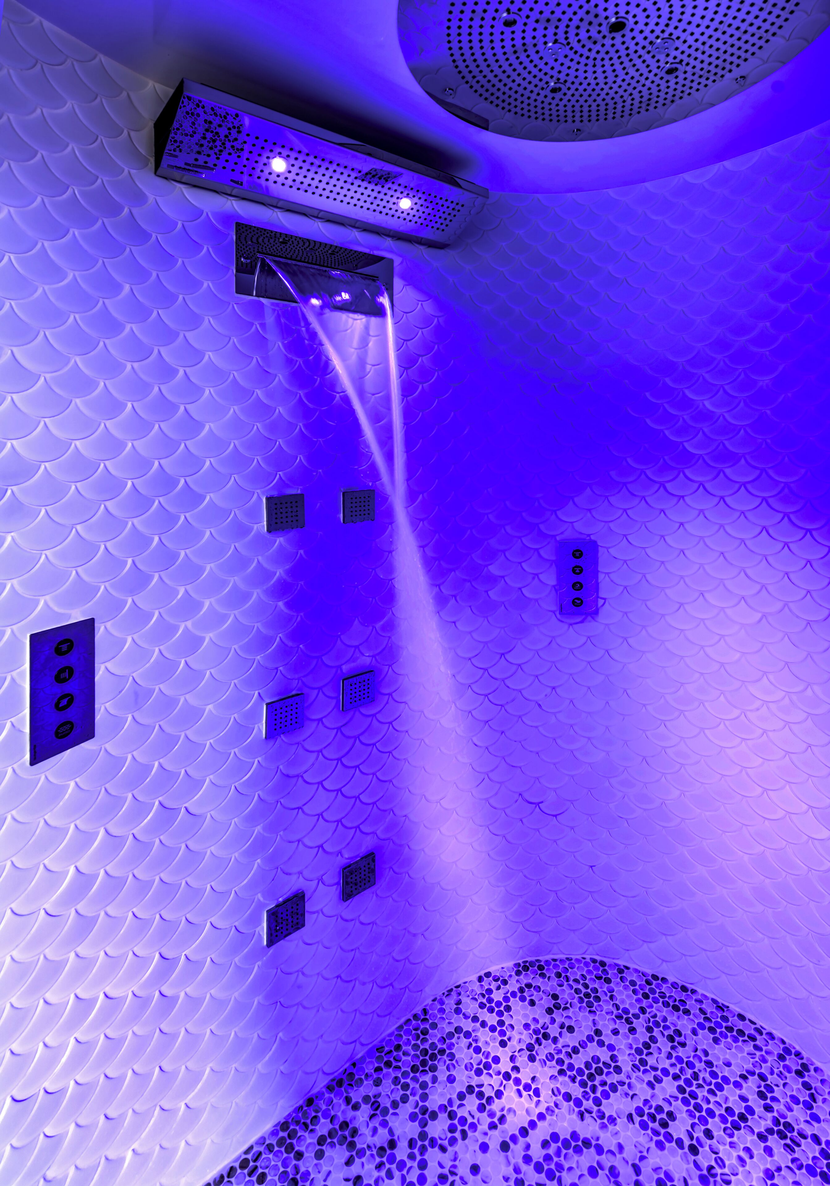 A room with a unique fish-scale textured wall, a ceiling with a circular pattern, and a series of small, evenly spaced vents.
