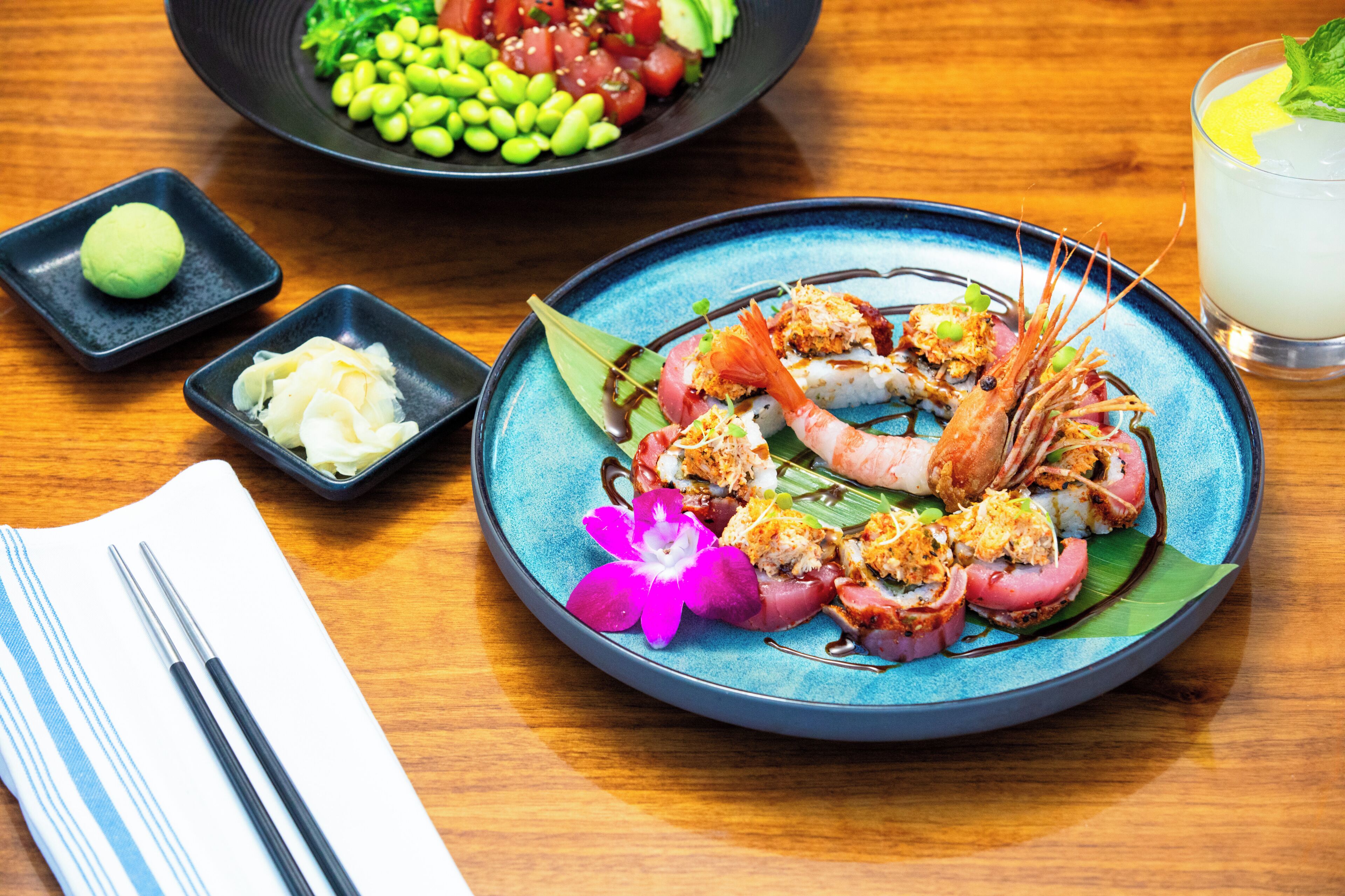 A table with a plate of sushi, a bowl of edamame, and a glass of drink.