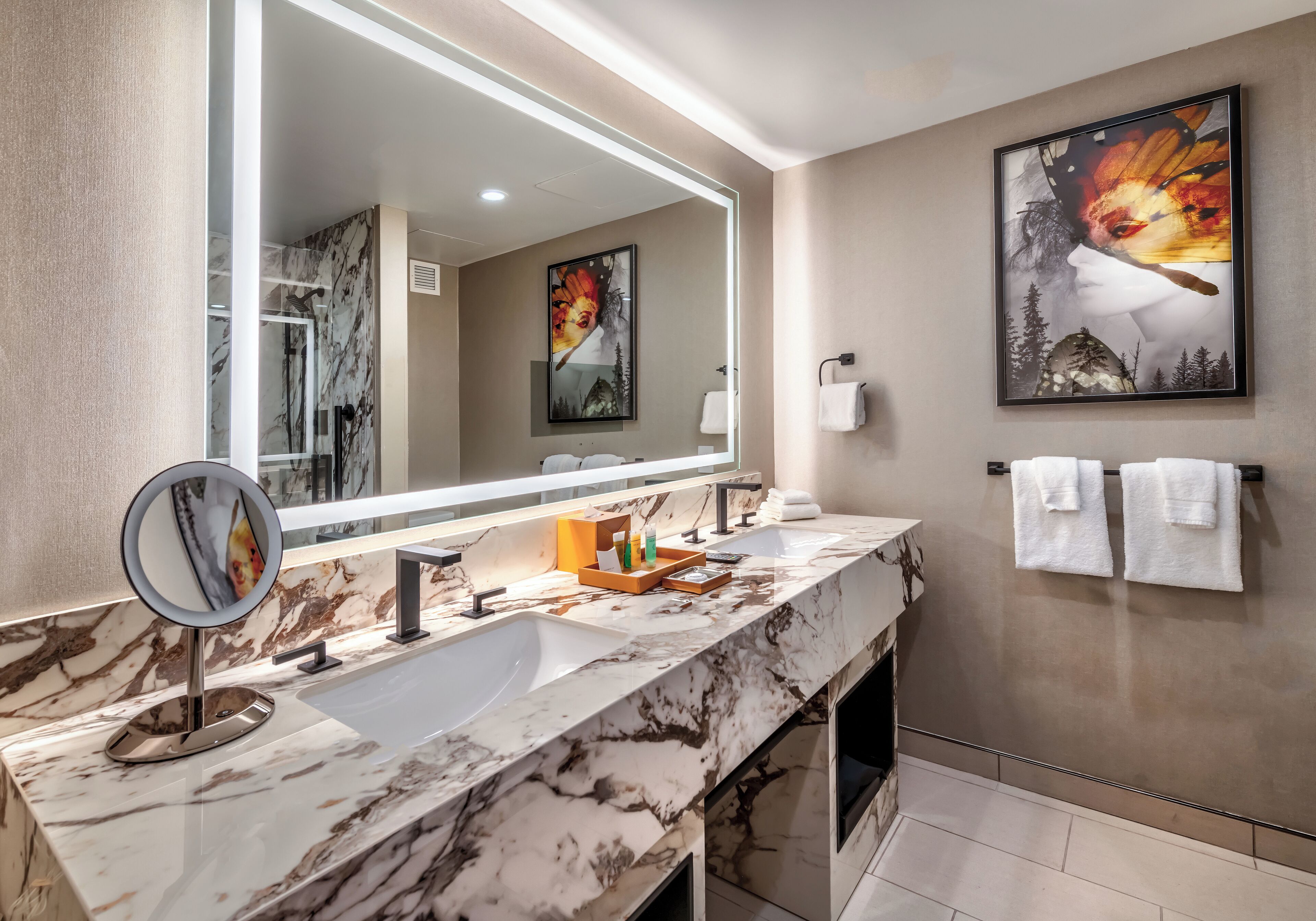 A bathroom with a marble vanity, a large mirror, two sinks, and a framed artwork on the wall.