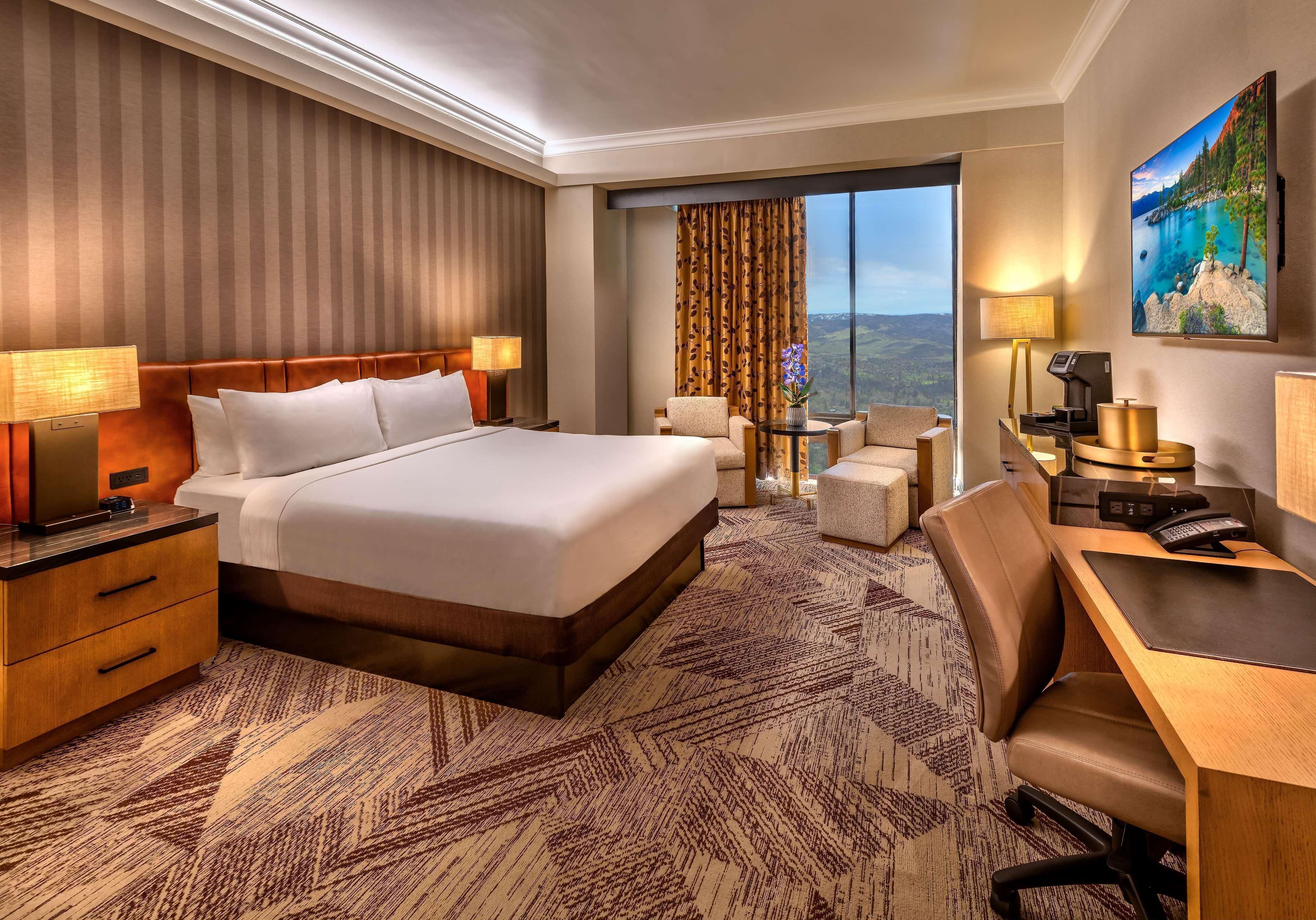 A hotel room with a large bed, a desk, a chair, a small table, and a view of the outdoors.