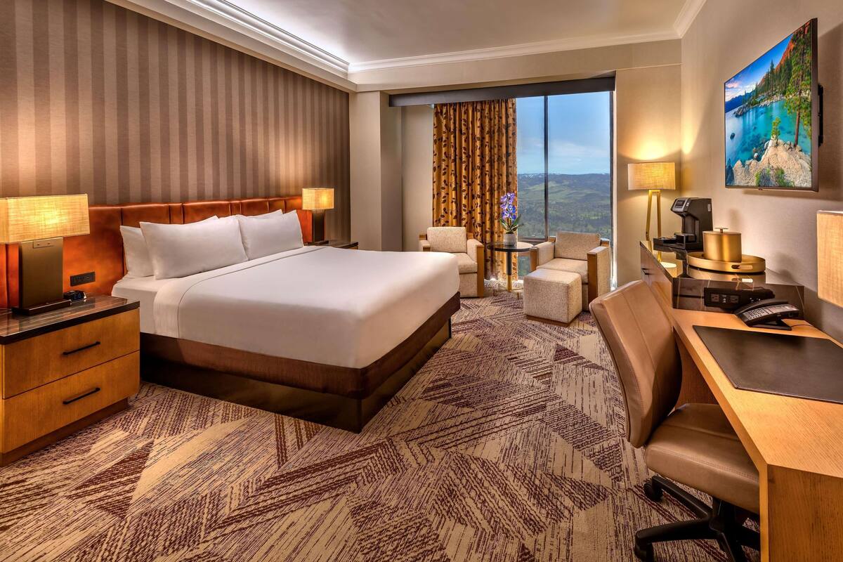 A hotel room with a large bed, a desk, a chair, a small table, and a view of the outdoors.